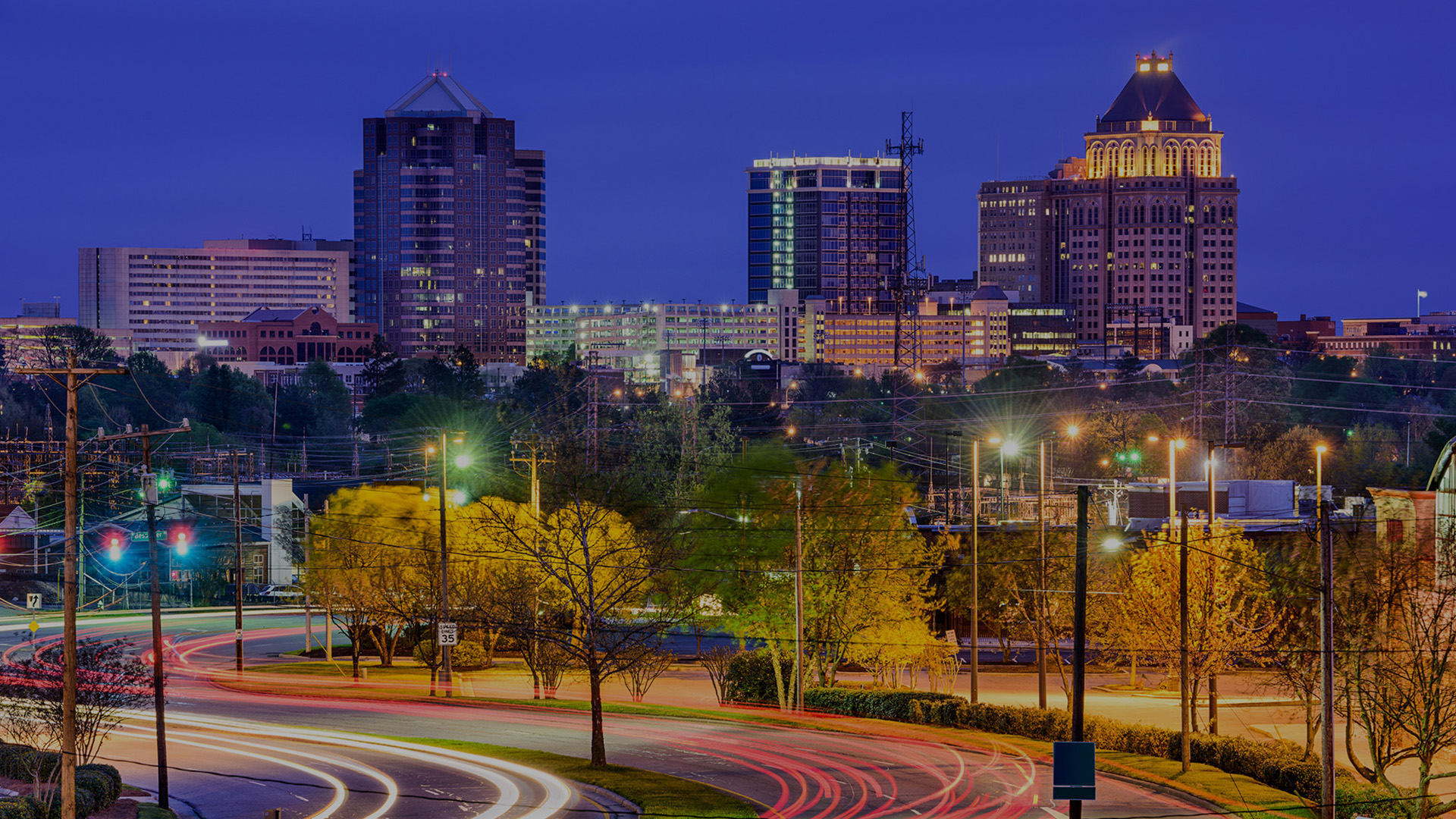A cityscape at night with a prominent skyline, illuminated buildings, and a streetlight-lit road curving around the scene.